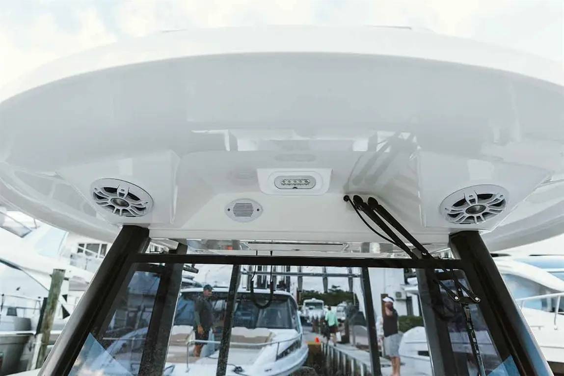 Interior view of a boat's overhead control panel featuring speakers, lights, and nearby boats in the marina.